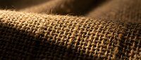 Natural burlap fabric texture with warm lighting showcasing woven jute fibers for rustic crafts and eco-friendly packaging applications.