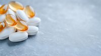 White pharmaceutical tablets and orange omega-3 fish oil capsules on gray concrete background with copy space for medical and healthcare concepts.
