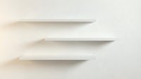 Three minimalist white floating shelves mounted on cream wall creating clean modern storage solution for contemporary interior design and home organization.