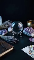 Crystal ball with amethyst geodes, tarot cards, lavender and singing bowl on dark surface for fortune telling and spiritual practices.