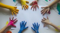 Colorful painted hands of children arranged in circle on white paper background, representing unity, creativity, and collaborative art education.