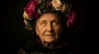Elderly Caucasian woman wearing a floral crown of roses and peonies, dark dramatic background, expressive portrait with cultural folk style.