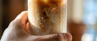 Close-up of a hand holding a glass of cold beverage with condensation and ice, perfect for refreshment and drink advertising campaigns.