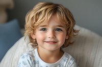 Young boy with blonde curly hair and blue eyes smiling at camera, wearing light colored shirt. Portrait suitable for family, parenting, childcare, education and lifestyle content.