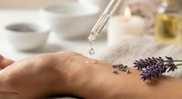 Aromatherapy massage with lavender essential oil drops from pipette onto woman's hand creating relaxing spa wellness treatment experience.