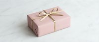 Pink gift box wrapped with elegant gold ribbon bow on white marble surface, perfect for holiday, birthday, and celebration concepts.
