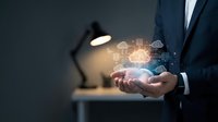 Businessman in suit holding glowing digital network icons and connected nodes in open palms, representing cloud computing, data connectivity, and technology innovation.