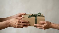 Hands exchanging wrapped kraft paper gift box with green ribbon bow against neutral background, suitable for holiday, celebration, generosity, and giving concepts.