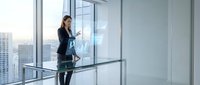 Professional businesswoman using smartphone in modern glass office with city skyline view during daytime for corporate communication and networking.