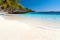 Pristine white sand beach with crystal clear turquoise water, palm trees and limestone cliffs creating secluded tropical paradise cove on sunny summer day.