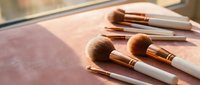 Professional makeup brushes with rose gold ferrules arranged on marble surface in warm natural light for beauty and cosmetics applications.