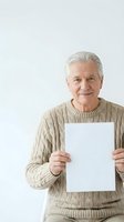 Senior man with gray hair and Caucasian ethnicity wearing beige cable-knit sweater holding blank white paper sign against neutral background for advertising and marketing campaigns.