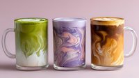Colorful marble effect drinks in glass mugs - green matcha latte, purple berry smoothie, and caramel coffee on pink background.