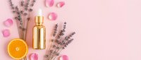 Luxury skincare cosmetic bottle with lavender flowers, orange slice and rose petals on pink background. Natural beauty products spa concept.