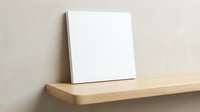 Blank white canvas on wooden shelf against beige wall for art projects and creative presentations.