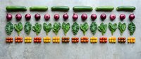 Fresh organic vegetables arranged in colorful rows including green beans, radishes, leafy greens and cherry tomatoes on white marble surface for healthy cooking.