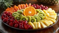 Fresh fruit platter with vibrant sliced kiwi, orange, pineapple and raspberries arranged in colorful pattern on dark plate, healthy food styling for catering.