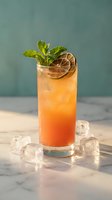 Refreshing orange cocktail with mint garnish and lime wheel in tall glass surrounded by ice cubes on marble surface for summer beverage menus.