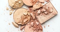 Broken makeup powder compacts in neutral beige and pink tones scattered on white background. Cosmetic products for beauty and fashion industry.