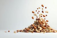 Mixed nuts and seeds falling into pile on white background, including almonds, cashews, and walnuts. Dynamic food composition with floating elements.