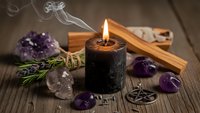 Mystical altar setup with burning black candle, amethyst crystals, sage bundle and wooden pentagram for spiritual rituals and meditation practices.