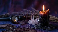 Black candle burning with flame surrounded by crystals, tarot cards and mystical objects on dark surface for spiritual rituals and fortune telling practices.