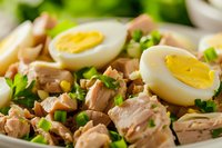 Fresh tuna salad with sliced hard-boiled eggs, chopped green onions and parsley on white plate, macro food photography for healthy meal recipes.