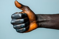African American male hand showing thumbs up gesture against light blue background, painted in black color with natural skin tone palm visible.