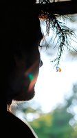 Silhouette profile of bearded man gazing at small colorful pendant against soft bokeh background with pine branches overhead creating atmospheric mood.