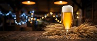 Golden beer glass with frothy foam on rustic wooden table surrounded by wheat stalks in warm pub atmosphere with bokeh lights for brewery marketing.