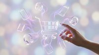 Hand reaching toward glowing digital shopping cart with floating e-commerce icons including smartphones, headphones and payment symbols on bokeh background.