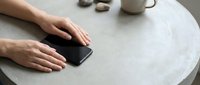 Hands reaching for smartphone on round table with coffee cup in background, modern lifestyle and communication technology concept for digital connectivity.