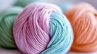 Colorful gradient yarn balls in pastel pink, blue, green, and peach tones arranged together, showcasing soft textile textures for knitting and crochet projects.