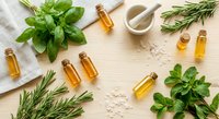 Natural essential oil bottles with fresh herbs basil rosemary on wooden background. Aromatherapy spa wellness concept with mortar pestle and sea salt crystals.
