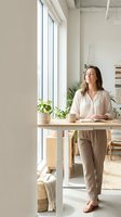 Young woman enjoying peaceful moment in bright modern home office with plants and natural light streaming through large windows.