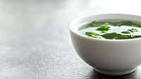 Fresh green herb soup in white ceramic bowl with parsley garnish on textured gray surface for healthy dining and culinary presentations.
