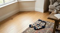 Young child wearing navy and white checkered socks sitting on ornate area rug in bright living room with wooden flooring, white baseboards and natural window light for home lifestyle content.