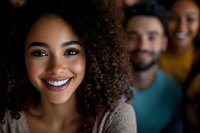 Young African American woman with natural curly hair and bright smile in foreground, with diverse friends blurred in background, expressing joy and friendship.