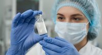 Female healthcare professional in protective equipment examining medical vial in laboratory setting for pharmaceutical research and development.