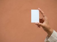 Hand holding blank white card against warm beige background, suitable for business branding, marketing mockups, and promotional material design.