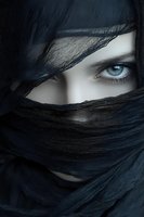 Mysterious woman with striking blue eyes wrapped in dark fabric veil creating dramatic portrait with intense gaze and cultural fashion styling.