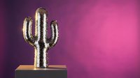 Golden metallic cactus sculpture on wooden base against vibrant purple pink gradient background for modern home decor and desert themed interior design.