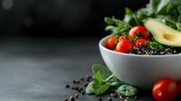 Fresh healthy bowl with cherry tomatoes, avocado, quinoa, and green leaves on dark background. Clean eating concept for food blogs and recipes.