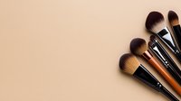Professional makeup brushes arranged in fan shape on beige background, soft bristles detail showing quality cosmetic tools for beauty application.