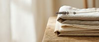 Stack of neatly folded beige and cream colored linen towels on wooden surface in bright minimalist bathroom interior for spa and home decor concepts.