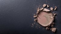 Crushed brown eyeshadow powder with scattered fragments on dark slate background for makeup and cosmetics applications.