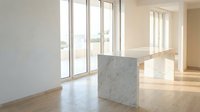 Modern minimalist kitchen island with white marble base and wooden countertop in bright contemporary home interior with large windows and natural light.