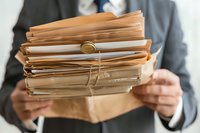Business professional holding stack of manila folders and documents with rubber bands, representing office paperwork and file organization in corporate setting.