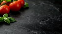 Fresh ripe cherry tomatoes and aromatic basil leaves on dark slate stone background with water drops and copy space for food photography.