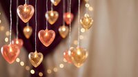 Golden heart-shaped ornaments hanging with warm bokeh lights creating romantic atmosphere for Valentine's Day, wedding or love celebration decor.